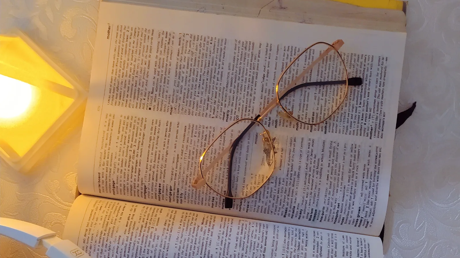 An open book and reading glasses rest beside a warm bedside lamp.